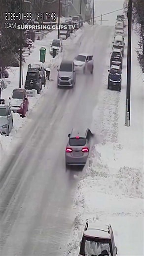 The video opens on a steep hill coated in a thick layer of ice, filmed from a stationary phone as winter conditions worsen. Snow lightly falls while the road glistens like glass under the cold light. One car cautiously attempts to descend, but almost immediately begins sliding sideways, tires offering no resistance. Seconds later, another vehicle enters the hill and loses control as well, drifting helplessly downhill. One after another, more cars follow, each sliding faster as gravity takes over