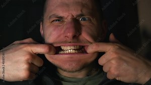 A man stretches his mouth with his hands. Wide-open mouth. Creepy facial expression. A frightening appearance of a man with a wide-open mouth.