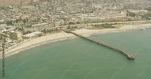 Helicopter aerial shot moving around beach pier, cloudy day