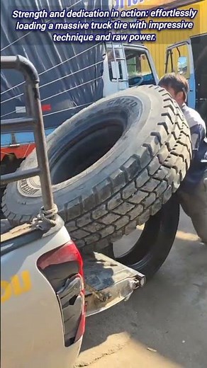 💪 Man single-handedly lifts giant truck tire onto flatbed.