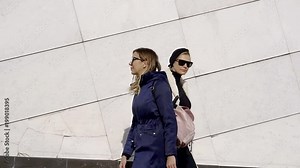 two women are approaching to each other on street near large white wall, looking and moving forward