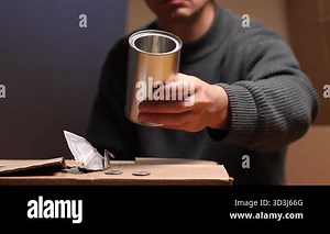 Unrecognizable homeless man sitting on cardboard, holding an empty tin can with coins and an origami crane dollar note, begging for charity and support on the street Stock Video Footage - Alamy