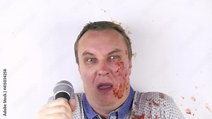 In slow motion, a tomato smashed against a young man's face during his performance.He wipes his face and grimaces. the man cries.