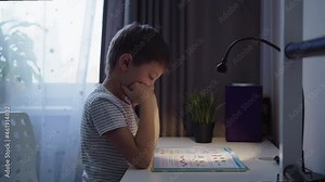 Little boy doing homework at home. kid reading a book at the table by the light of lamp. High quality FullHD footage