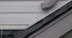 During a heavy downpour, a metal gutter overflowing with rainwater pours down a home's exterior. The gutter appears securely fastened to the building's wall.