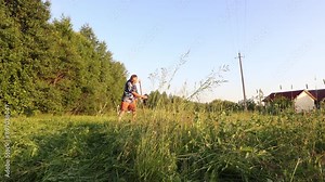 Using steel scythe with wooden shaft to cut grass in an agricultural field, farmer in Hawaiian Shirt makes hay during haymaking.