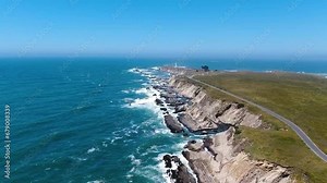 Aerial video of a rocky beach coast with a road on the right side along with a blue ocean. Drone goes forward, leading to the distant horizon in Bodega Bay, California