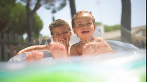 Two little brothers playing together in the pool on a sunny day of summer, in a sweet and happy way