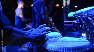 Conga drummer playing at stage on festival with band. Congo player performs on concert. Percussion instrument. Congas. Musician's hands playing music.