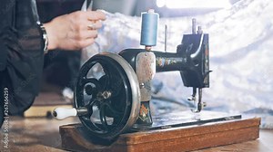 Old black sewing machine on the background of a female tailor at work in atelier. Professional seamstress working in the workshop with beautiful material.