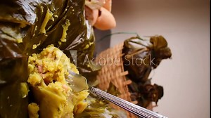 Vertical video of a hand taking a traditional Colombian food known as "tamal" wrapped with leaves from a basket on a black table