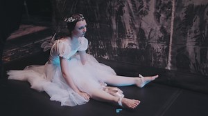 A ballerina stretches her legs while sitting backstage and looking at the stage. The ballet dancer is preparing for a performance. Professional ballet.