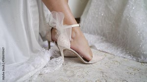 Bride tying shoes with delicate ribbons Close-up of hands and sparkly heels Lace dress and feather details visible Preparing for a wedding ceremony Elegance and bridal fashion elements