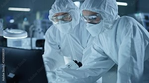 Research Factory Cleanroom: Engineer and Scientist Wearing Coveralls Talk and Work on Computer, Use Microscope to Inspect Motherboard Microprocessor, Develop Electronics for Medical Electronics