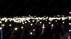 Defocused spectators in hall with lights waving in the dark. Action. Audience holding phones with shining flashlights during the concert, romantic atmosphere.