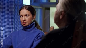 Adult 44 year old woman having lively conversation with elderly woman sitting at table in living room. Woman with tense face talks, elderly woman listens.