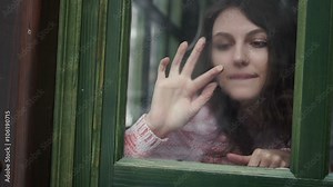 beautiful girl sitting on the window sill and painting on glass