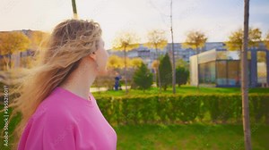 Close-up female legs walk along sidewalk street of modern city. Woman walking in public park, back light sunset light spring nature outside green grass summer trees. Girl in pink sneakers blue jeans