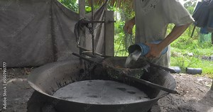 close-up of a toddy-tapper pouring freshly harvested palm sap in a huge pot using a strainer