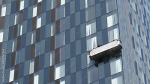 Unrecognizable window washers on hanging suspended scaffolding platform washing checkered high rise building glass wall.