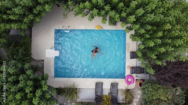 Young couple enjoying summer by the pool - drone hovers over pool in bird's eye view. The man spins the woman on the water, like Watsu