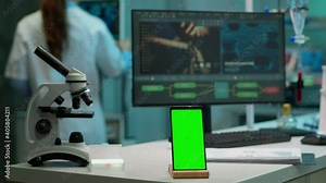 Display phone with green screen, mock up on template placed on desk in scientific lab while team of medical researcher scientists analysing virus evolution at digital monitor conducting experiment