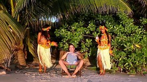 Two Hawaiian hula dancers dancing around a fat man resting in a retro swimsuit on the sea beach on a background of palm trees