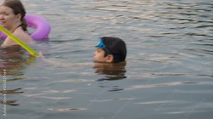 happy children, boy and girl swim in a forest lake. splashing each other. play. enjoying vacations and outdoor recreation. in blue water at sunset; bathe in lake or river and making water drops