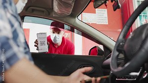 smiling gas station attendant collecting payment through window from young man at driver seat paying with credit card or qr code chatting with him.