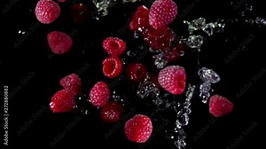 Ripe juicy raspberries with water bouncing against to the camera on a black background in slow motion super close-up