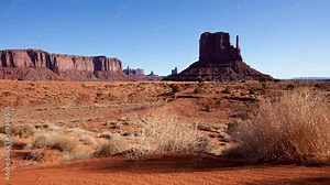 Time Lapse of sunlight and shadows moving across Monument Valley at sunrise. Camera moves past tumbleweeds with the buttes of Monument Valley in the background.