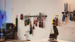 Close up of electric router on workbench in assembly shop with woodworking tools on rack in background. Focus on hand powered gear used for cutting wood in carpentry studio, panning shot
