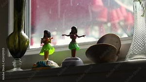 Small solar powered hula dancer figures dance in dark room in front of window at daytime.