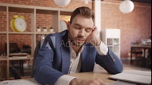 A young man in the office sleeps at the table, then wakes up and starts sorting through documents and writing in a notebook. Slow motion 4k footage