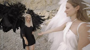 Black and white angels. Young women dressed as white and black angels with wings hold out their hands to each other.