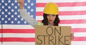 Female construction worker holds On Strike sign shaking fist against American flag. Female represents determination and struggle for labor rights