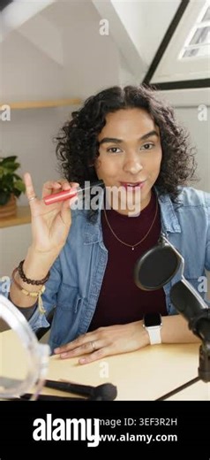 Vertical video: Non-binary creator lifting red gloss tube at loft desk, twisting cap to reveal wand. Cosmetics, beauty, lifestyle, modern, creative, self-care, vertical video Stock Video Footage - Alamy