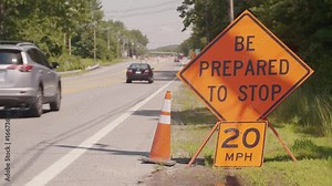 Safety orange roadwork construction sign with passing traffic. Be Prepared To Stop, 20 mph Stock Video