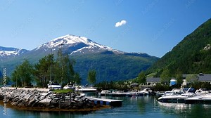 Beautiful boat marina harbor at Valldal, Norway on the calm waters of a fjord on a sunny day with snow on the peaks of the spectacular nearby mountains as a seagull flies by. Breathtaking beauty!