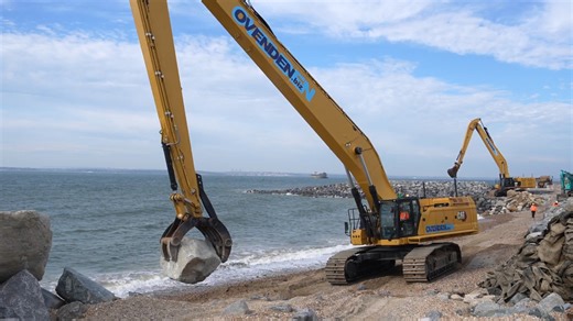 Massive excavator lifting giant rocks by the sea