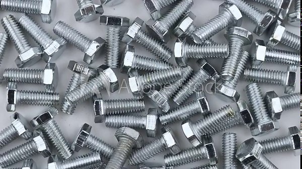 A scattered of stainless M6 threaded bolts. Movement with rotation. Close-up, flat lay, top view.