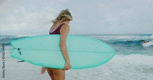 Beautiful surfer girl running down the beach into the ocean
