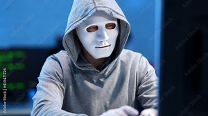 Caucasian hacker in white mask and gloves coding indoors and waving at camera. Unrecognizable man hacking internet website or coding computer virus. Programming concept.
