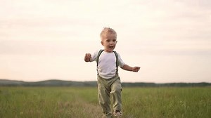 Joyful child walking on green grass in the park. Child enjoys a peaceful escape from the bustle of the city. Little explorer child, walking on the green grass in park, discovers the wonders of nature