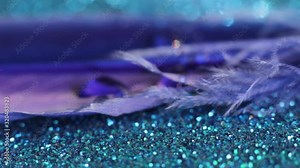 The blue feather rests on a shiny blue background, with drops of water falling on it