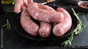 Chef puts plate with bratwurst or raw sausages on dark background with rosemary and spices for cooking. Oktoberfest food. 4k video