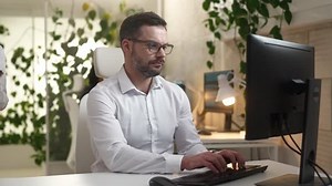 Young professional IT worker using computer sitting at table in office with young female asian manager approaching with tablet managing work of employees. Two colleagues working in company.