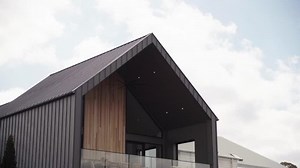 Exterior shot of a luxurious large house with a metal gabled roof and with a balcony and glass railing in front of a luxurious and expensive wooden wall