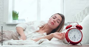 Beautiful sleepy girl lying in bed, turning off the alarm Clock and covering with Blanket in the Morning.Young Woman continues to sleep after Alam Clock, Lazy Morning. Home Quarantine. Staying Indoor.