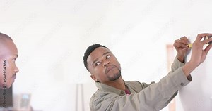 Happy african american gay male couple using tape measure and making mark on wall, slow motion
